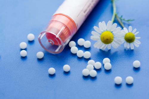 Chamomile flower and homeopathic medication on blue surface